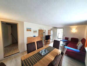 Ein Essbereich mit Holztisch und -stühlen, einem Schrank mit Gläsern, einem Fernseher und einem roten Sofa.