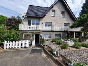 Ein zweistöckiges Haus mit weißem Zierzaun, Satellitenschüssel und einem Garten mit einem Kiesweg.
