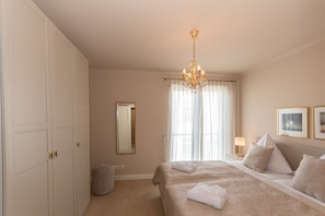 A bedroom with a bed, a chandelier, a mirror, and a bedside table with a lamp. - Villa Friede-Marie, App. Svea with harbor and Baltic Sea view - Villa Friede-Marie, App. (Sassnitz auf Rügen)