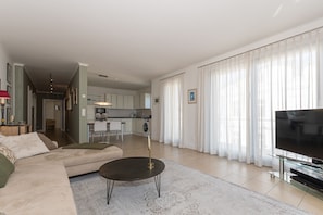 A modern living room with a sofa, a coffee table, a TV, and a kitchen in the background. - Villa Friede-Marie, App. Svea with harbor and Baltic Sea view - Villa Friede-Marie, App. (Sassnitz auf Rügen)