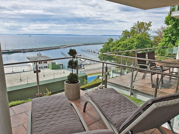 A balcony with a view of a harbor, a small tree, and outdoor seating. - Villa Friede-Marie, App. Svea with harbor and Baltic Sea view - Villa Friede-Marie, App. (Sassnitz auf Rügen)