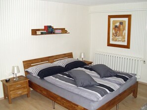 A bedroom with a wooden bed, bedside tables, a radiator, a framed picture on the wall, and a bookshelf. - Vacation apartment on the outskirts (Sassnitz auf Rügen)