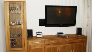 Ett vardagsrum med en platt-TV som är monterad på väggen, träskåp under och en hylla med dekorativa föremål.