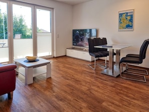 Ein modernes Wohnzimmer mit Fernseher, Esstisch, Stühlen und einem roten Sofa.