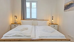 Ein Doppelbett mit weißer Bettwäsche, zwei Nachttische mit Lampen, ein Fenster mit Jalousien und ein Gemälde an der Wand.
