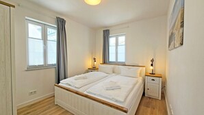 Un lit double avec du linge de lit blanc, deux tables de chevet avec des lampes et une fenêtre avec des rideaux.