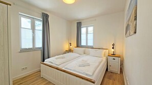 Ein Doppelbett mit weißer Bettwäsche, zwei Nachttische mit Lampen und ein Fenster mit Vorhängen.