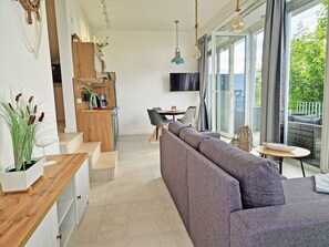 Ein stilvolles Wohnzimmer mit Küche, Essbereich und großem Fenster mit Blick auf Grünflächen.