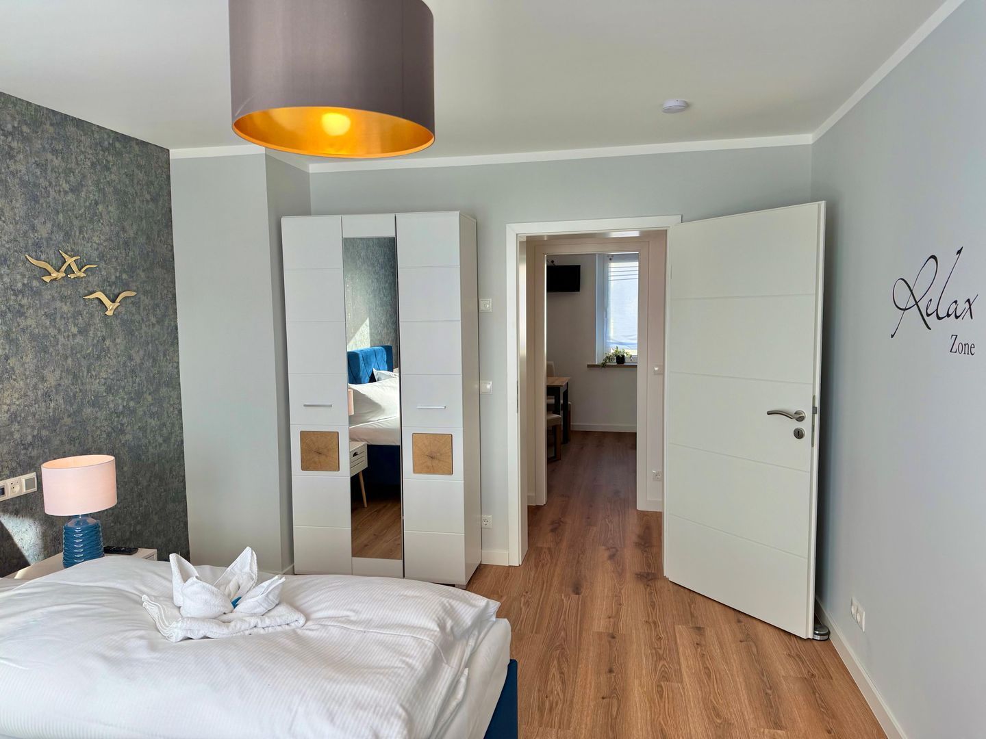 A hotel room with a bed, a mirror, a door leading to a bathroom, and a hallway.
