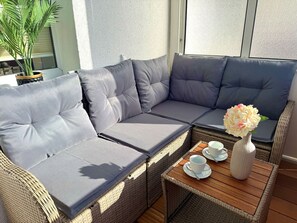 A wicker sofa with grey cushions, a small wooden table with cups and a vase, and a potted plant. - Vacation apartment Little Sea Lion (Sassnitz)