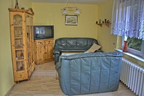 Ein Wohnzimmer mit einer Ledersofa, einer Holzkabine, einem Fernseher und einem Fenster mit Spitzenvorhängen.