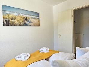 A hotel room with a bed, a painting of a beach, and a door leading to a bathroom. - Bädervilla Emma - Holiday apartment Ostseepanorama (Sassnitz auf Rügen)