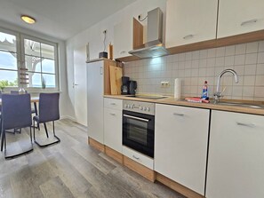A modern kitchen with white cabinets, a built-in oven, a coffee maker, and a sink. - Bädervilla Emma - Holiday apartment Ostseepanorama (Sassnitz auf Rügen)