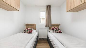 Ein kleines, sauberes Zimmer mit zwei Einzelbetten, einem Fenster mit Vorhängen und Holzschränken.