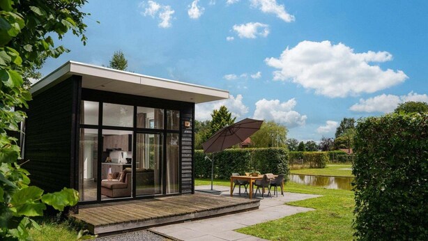 Una casa moderna con facciata in vetro, un patio in legno e un'area pranzo con tavolo e sedie.