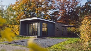 Ein modernes Haus mit einem großen Glasfenster, einer Holzterrasse und einem Kiesweg.