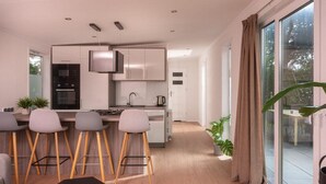 Eine moderne Küche mit Barhocker, einem Esstisch und einer großen Schiebeglasdoor zum Außenbereich.
