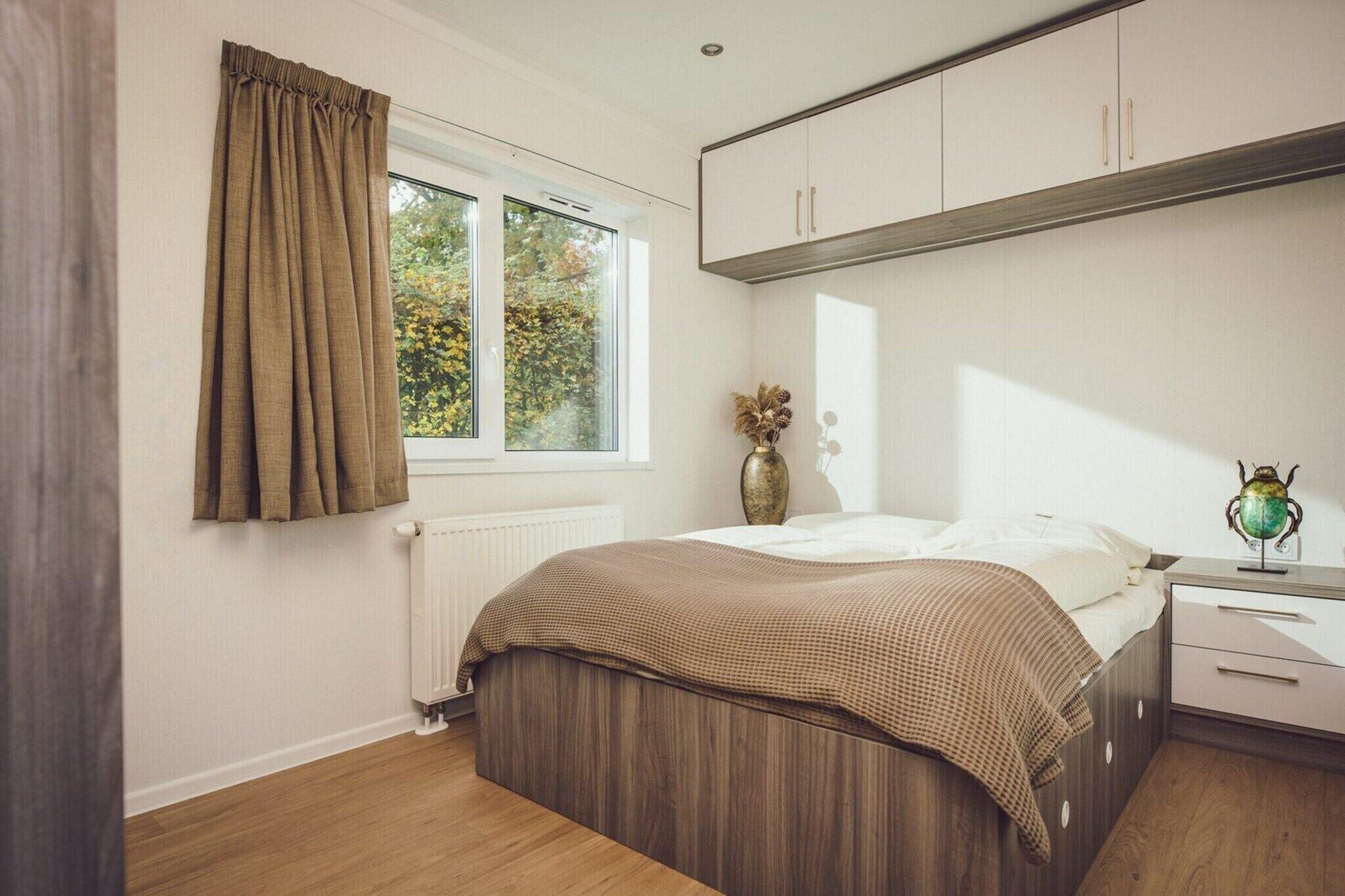 A bedroom with a bed, a nightstand, a dresser, a window with curtains, and a radiator.