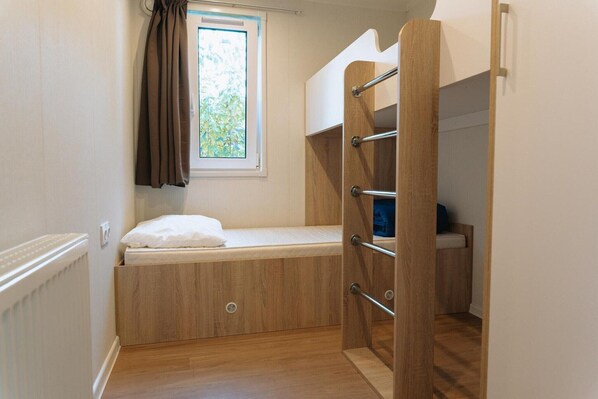 Quarto pequeno com beliche, janela com cortinas e radiador.