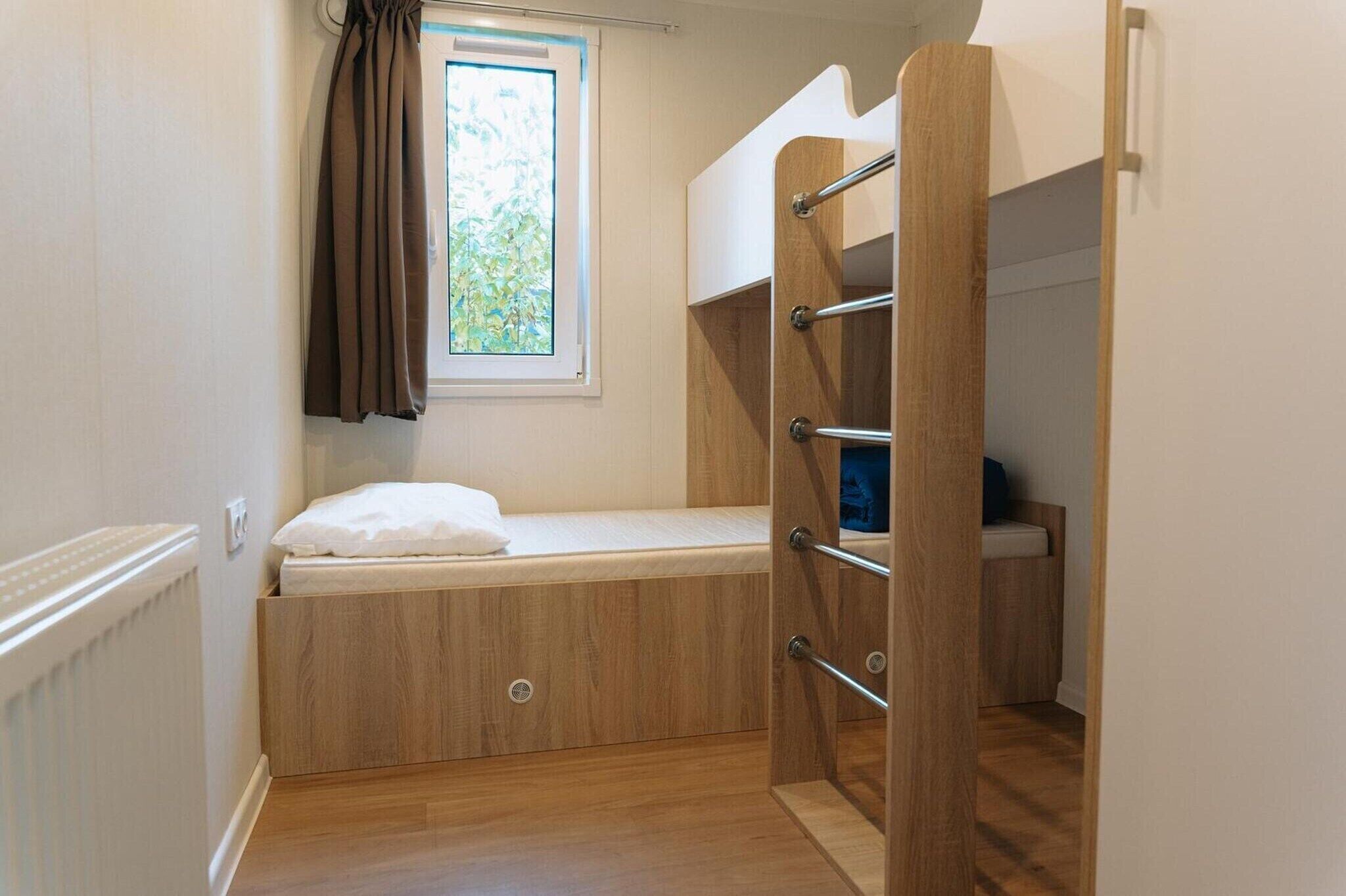 Una habitación pequeña con una cama litera, una ventana con cortinas y un radiador.