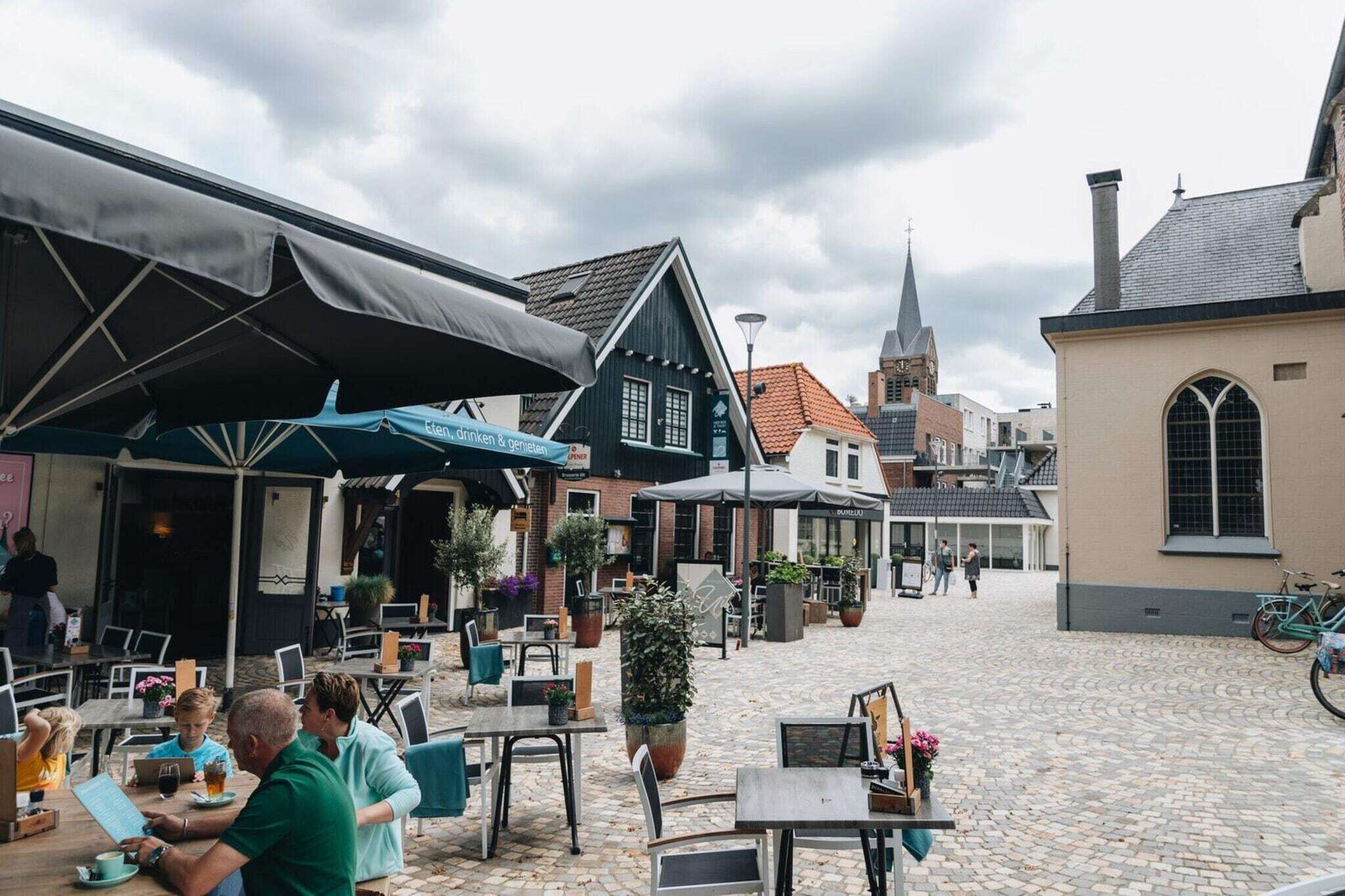 An outdoor café with tables and chairs, a cobblestone street, and historic buildings in the background.