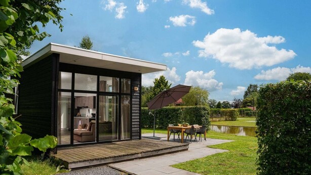 Ett modernt hus med en glasfasad, ett trädäck och en matplats med utemöbler.