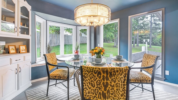 Een eetgedeelte met een ronde tafel, stoelen met luipaardprint, een kroonluchter en grote ramen met uitzicht op de omgeving.