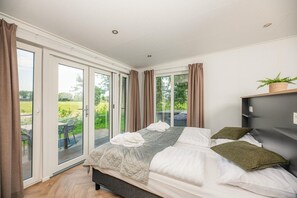 Un dormitorio con cama, mesita de noche, ventana con cortinas y vistas al exterior.