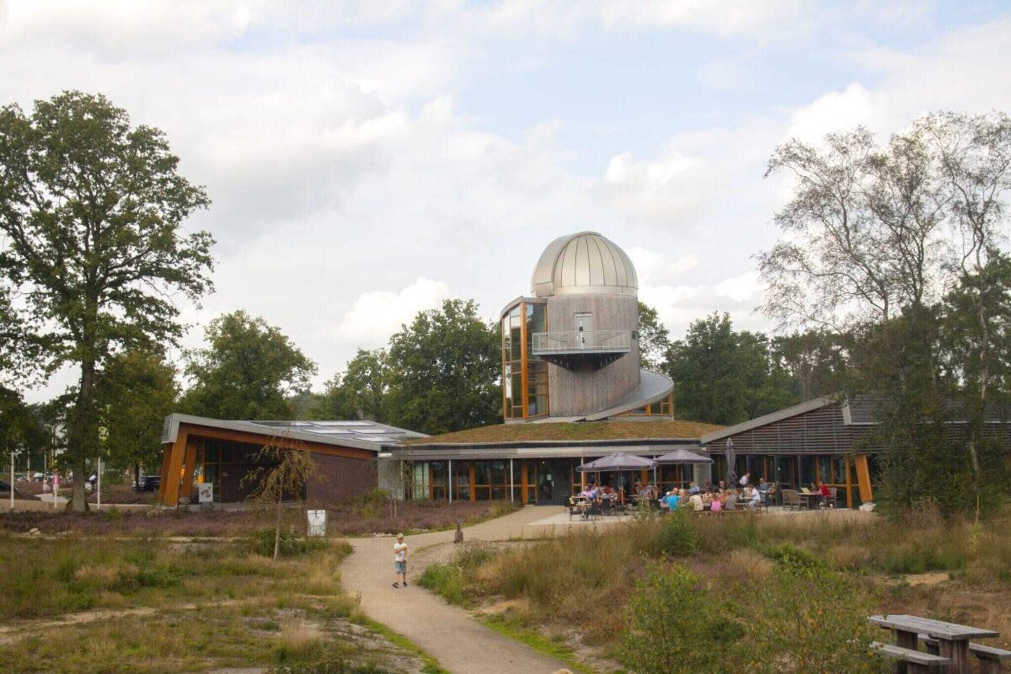 Ein modernes Gebäude mit Kuppelbauweise, einem überdachten Außenbereich und einem Weg zum Eingang.