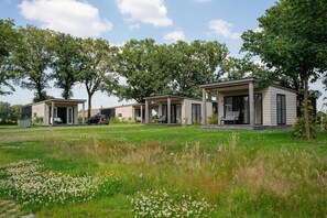 Una hilera de cabañas modernas de un piso, con porches abiertos, rodeadas por un campo cubierto de césped y árboles.