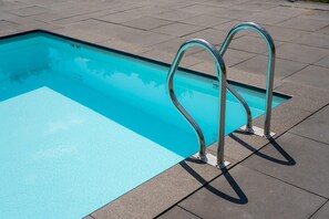 Una piscina rectangular con superficie de agua cristalina y azul, rodeada por un suelo de baldosas.