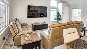 A modern living room with a large flat-screen TV, leather sofas, a wooden coffee table, and a potted plant.