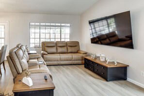 Een woonkamer met een leren bank, een houten salontafel, een aan de muur bevestigde televisie en een groot raam.