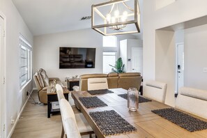 Een eetruimte met een lange tafel, comfortabele zitmogelijkheden, een kroonluchter en een televisie aan de muur.