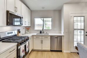 Een moderne keuken met witte kastjes, een RVS-fornuis, een magnetron en een vaatwasser.