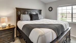 A bedroom with a bed, a nightstand, a lamp, a clock, and a window.