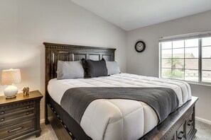 Quarto com cama, mesa de cabeceira, abajur, relógio e janela.