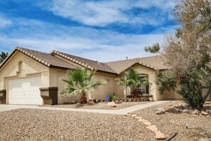 Een woonhuis met garage, oprit en een aangelegde tuin met palmbomen en rotsen.