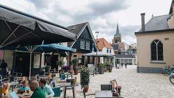 An outdoor café with tables and chairs, a cobblestone street, and historic buildings in the background.