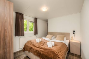 Ein Schlafzimmer mit Bett, Fenster mit Vorhängen, Nachttisch mit Lampe und Heizkörper.