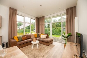 Un salon moderne avec un canapé d’angle, une petite table ronde et une grande fenêtre agrémentée de rideaux.