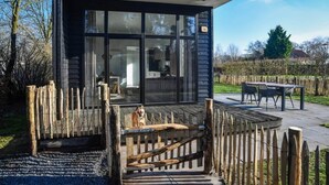 A modern house with a large glass window, a wooden deck, and a fenced area. - Pet-Friendly Forest Lodge with Fenced Garden (Rijssen)