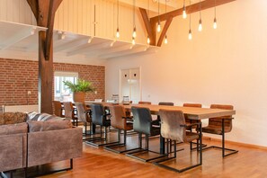 Un interior moderno con una larga mesa de madera, varias sillas, un sofá y lámparas colgantes.