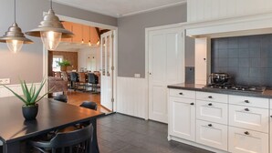 A modern kitchen with white cabinets, a black countertop, and a stove. There is a dining area with a table and chairs. - Retreat with Authentic Thatched Roof (Zuna)