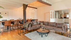 A spacious living area with a large sectional sofa, a dining table with chairs, and a kitchen in the background. - Retreat with Authentic Thatched Roof (Zuna)