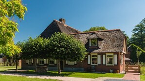 A traditional thatched-roof house with a brick extension, surrounded by trees and a clear sky. - Retreat with Authentic Thatched Roof (Zuna)