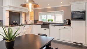 A modern kitchen with white cabinetry, a central island, a pendant light, and a window with a view. - Retreat with Authentic Thatched Roof (Zuna)