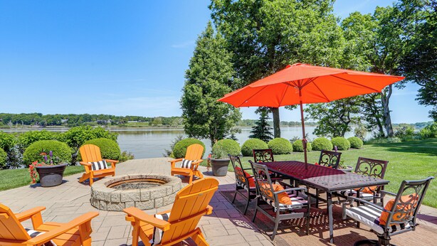 Eine Terrasse im Freien mit Adirondack-Stühlen, einer Feuerstelle und einem Tisch mit Sonnenschirm.