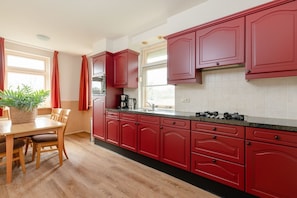 A kitchen with red cabinets, a wooden dining table, and a potted plant.