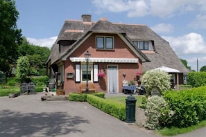 A traditional brick house with a thatched roof, a front porch, and a small garden.